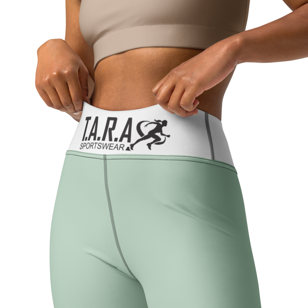 Woman in a yoga pose wearing a white sports bra and green leggings with 'TARA' branding on a white background