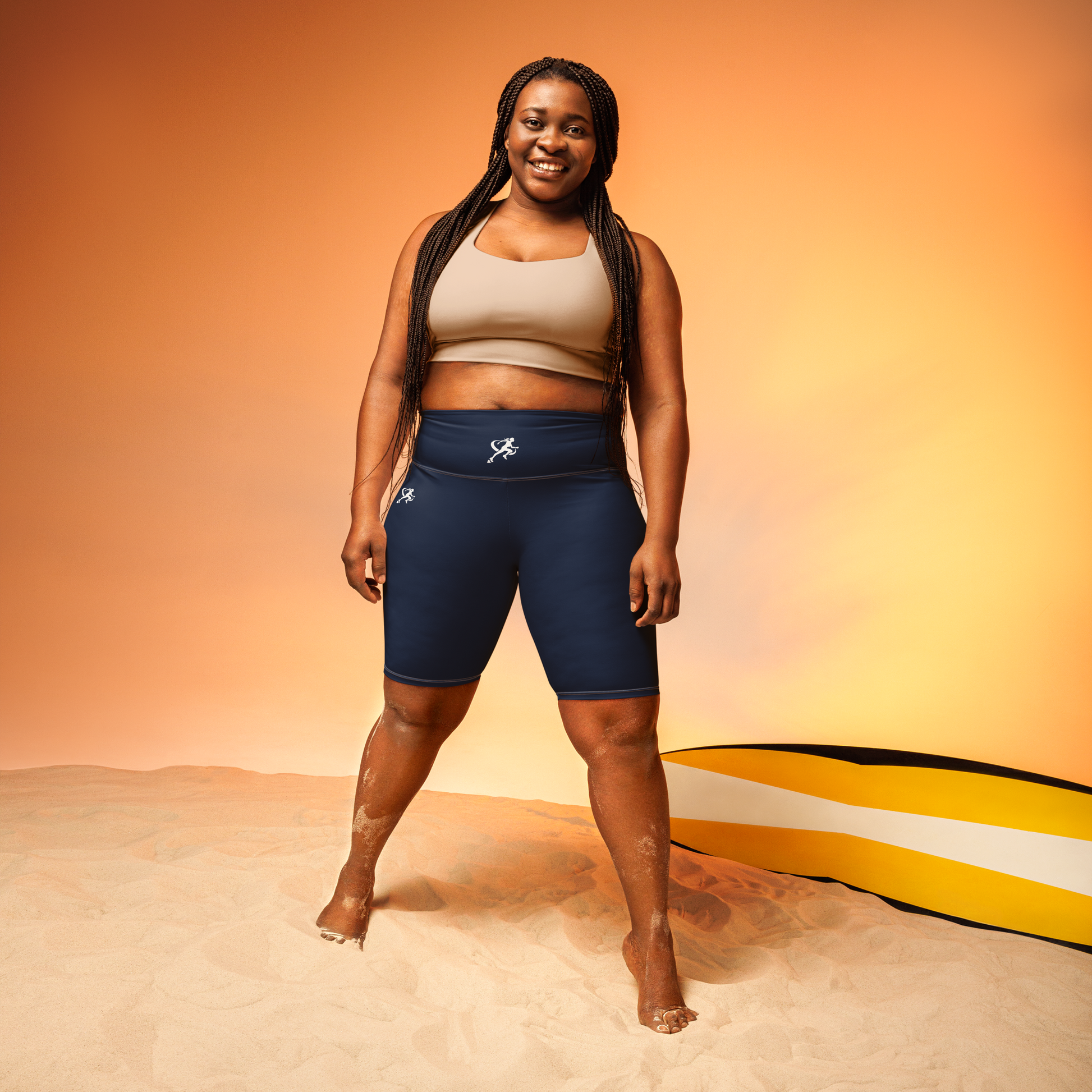 Woman wearing a sports bra and shorts standing on sand with a colorful background