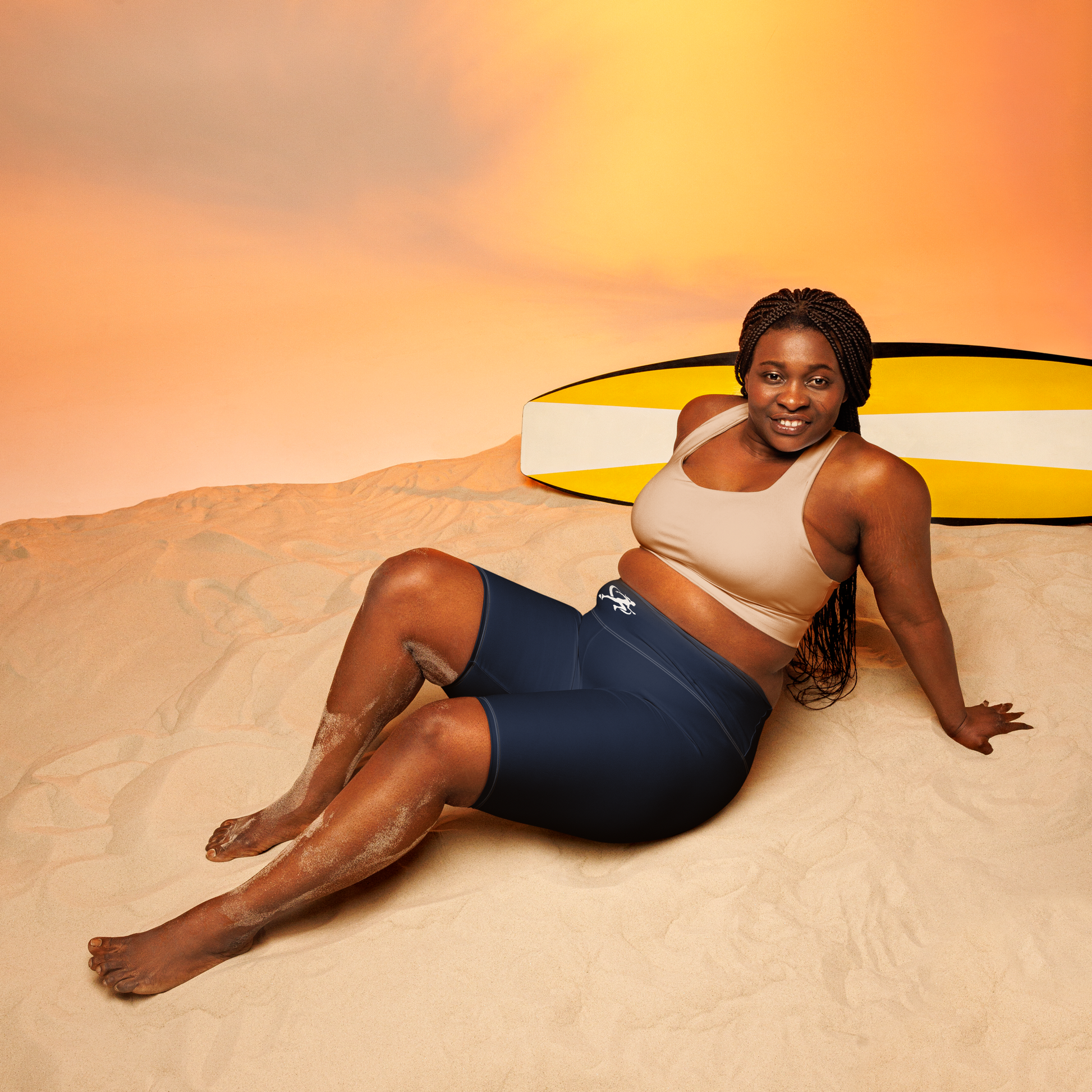 Woman wearing a sports bra and shorts standing on sand with a colorful background