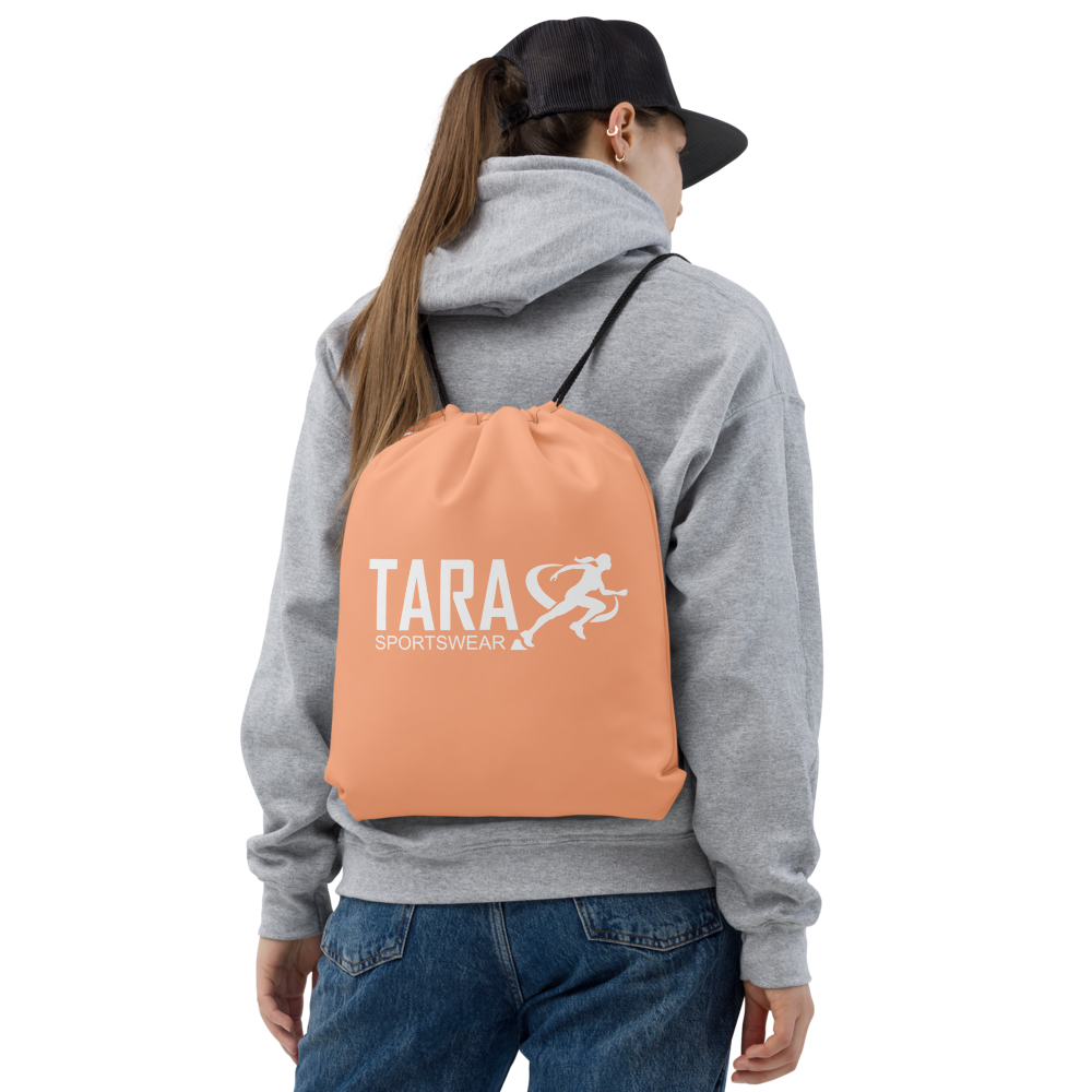 Person wearing a gray hoodie and blue jeans with a peach backpack featuring 'TARA SPORTSWEAR' on a white background