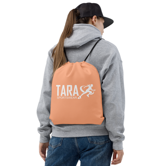 Person wearing a gray hoodie and blue jeans with a peach backpack featuring 'TARA SPORTSWEAR' on a white background
