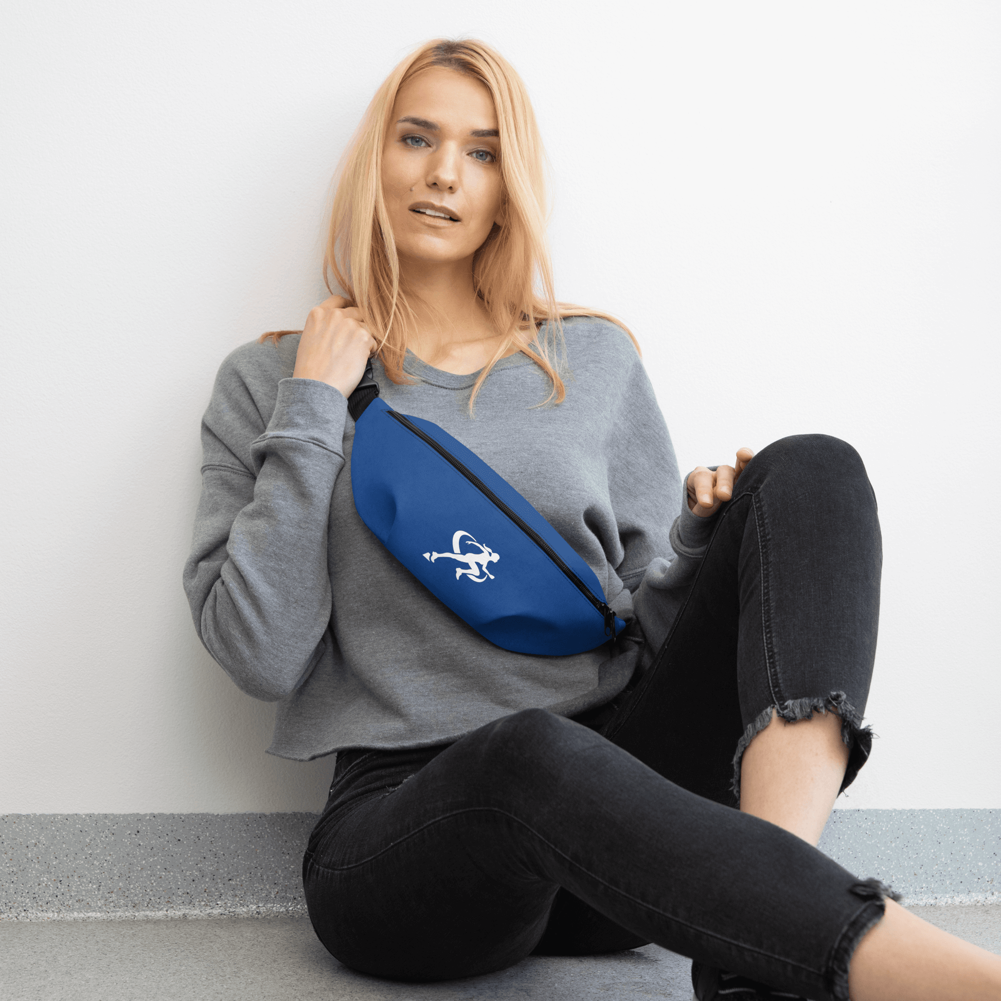 Woman sitting on the floor with a blue fanny pack featuring a logo.