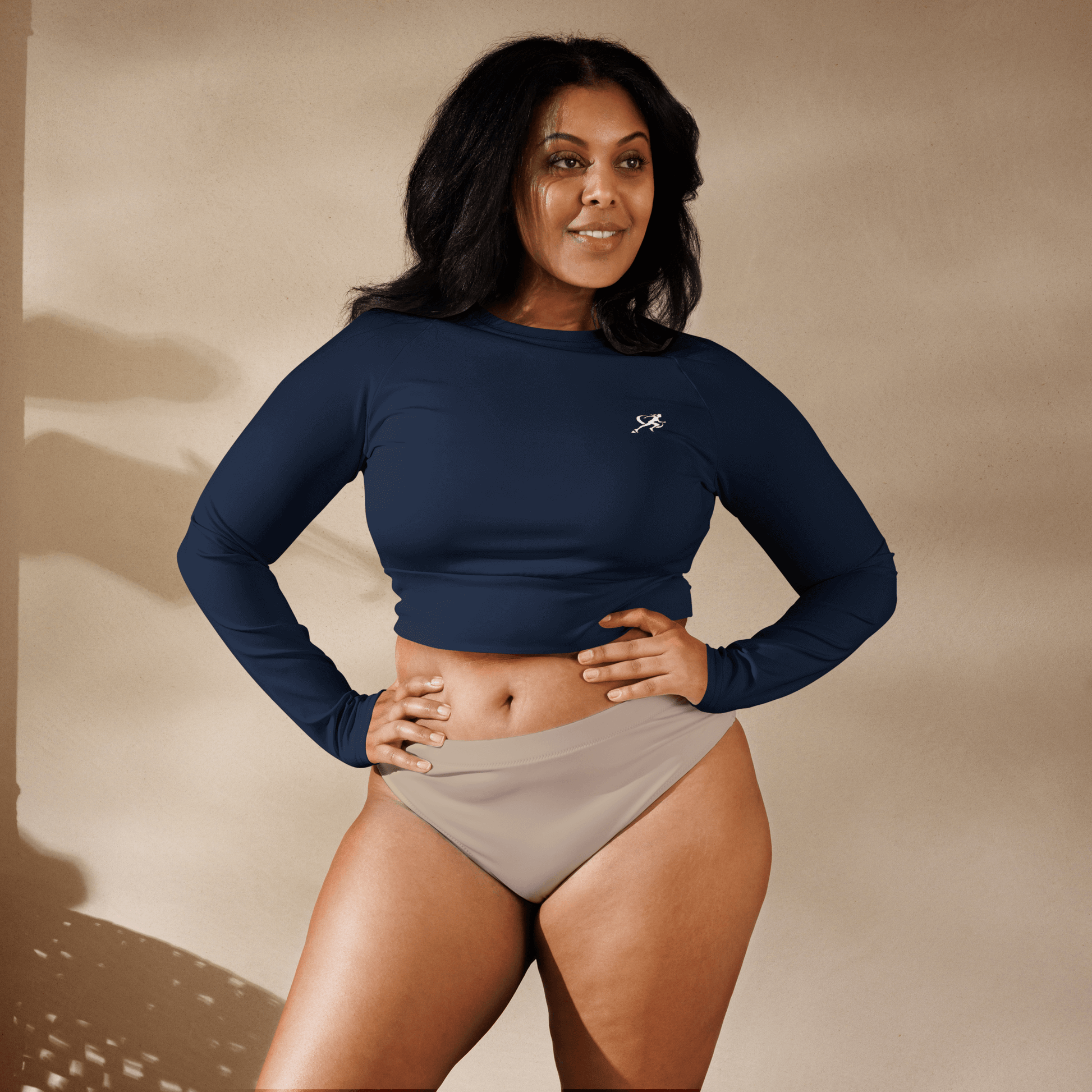 Woman wearing a navy long-sleeve top and beige shorts against a beige background
