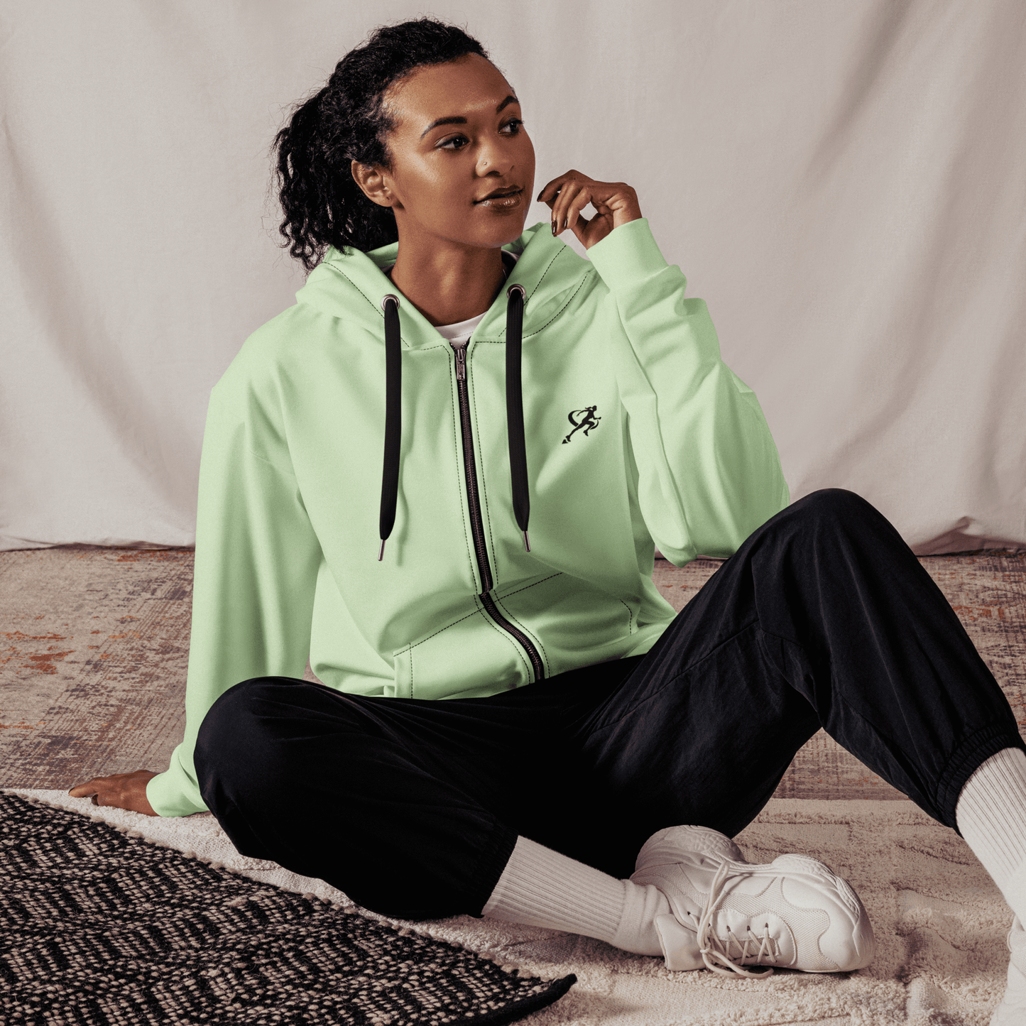 Woman wearing a light green hoodie with a logo on a white background