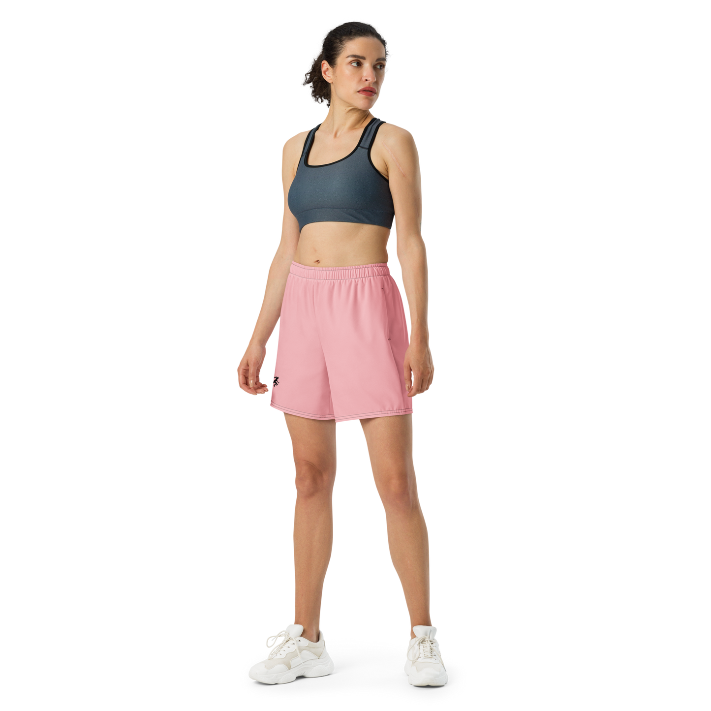 Woman wearing a dark sports bra and pink shorts on a white background