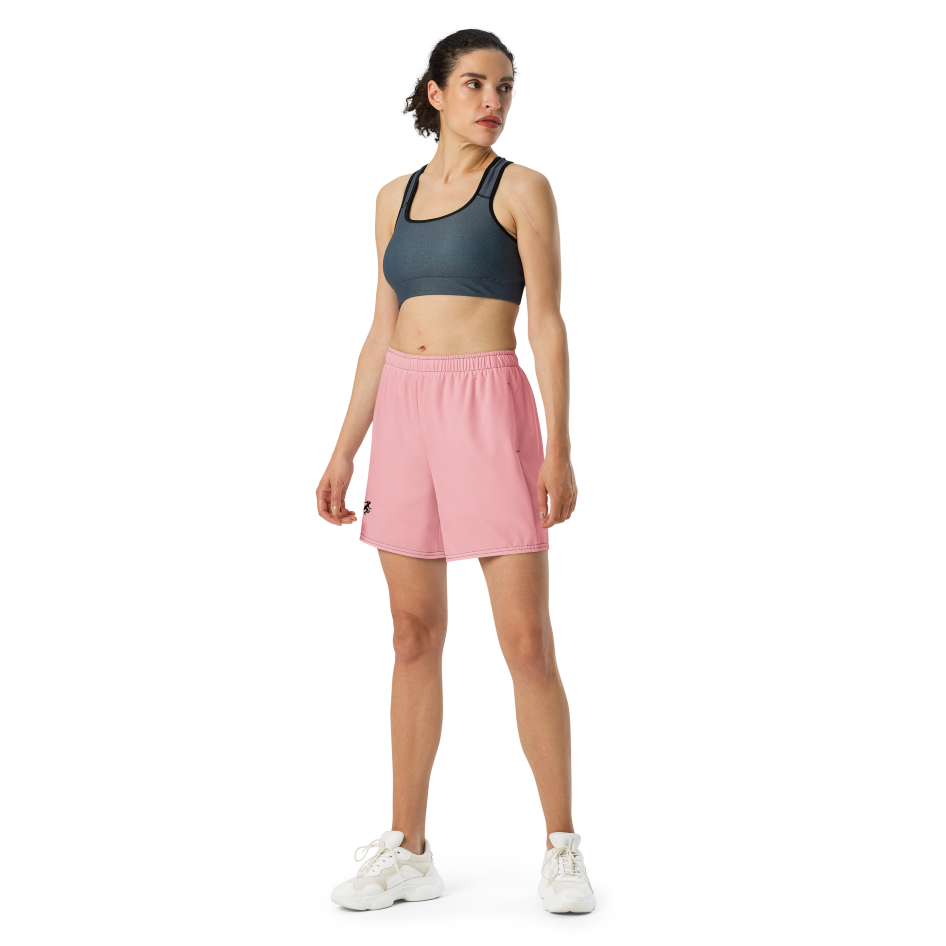 Woman wearing a dark sports bra and pink shorts on a white background