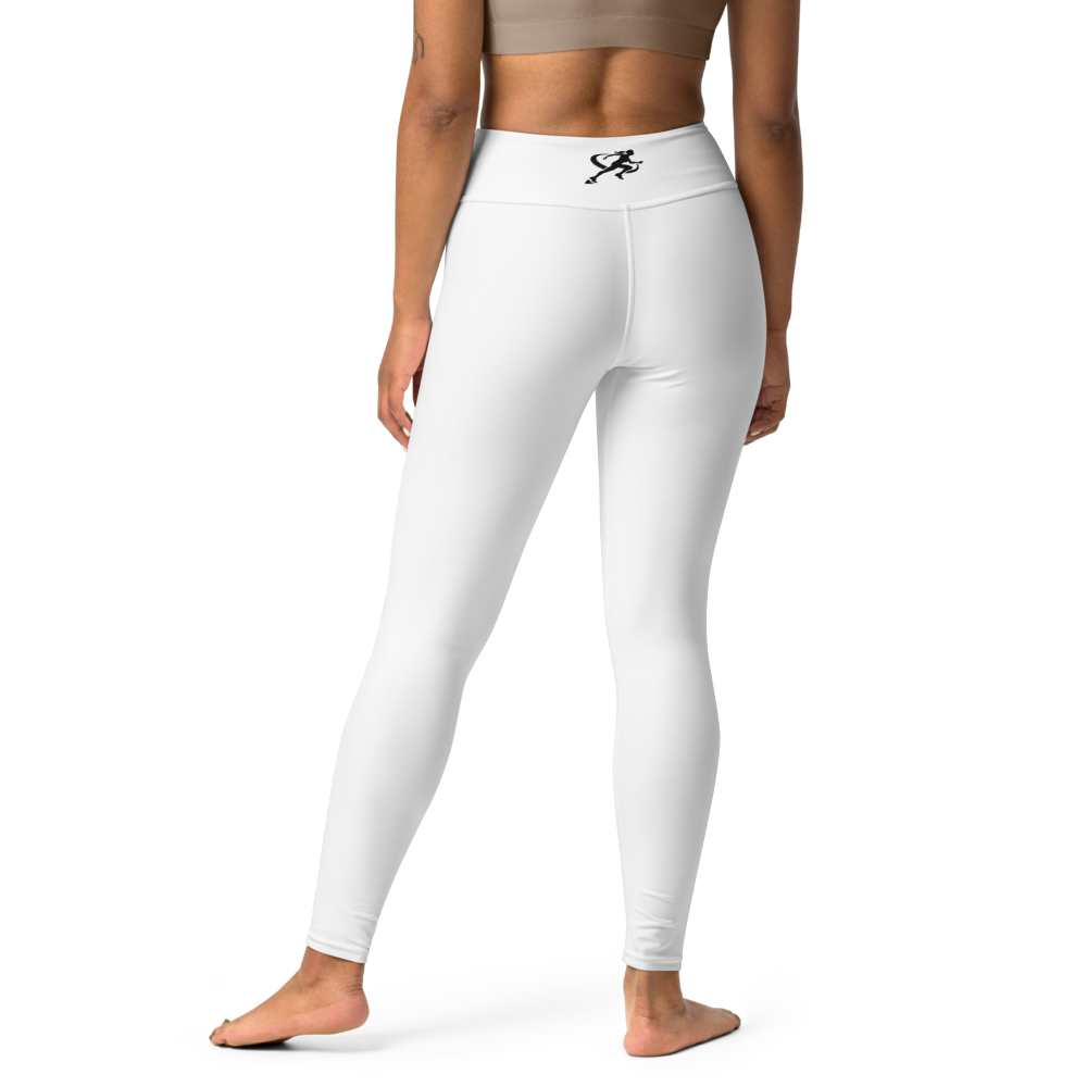 Woman wearing a sports bra and white leggings with a brand logo, standing against a neutral wall.