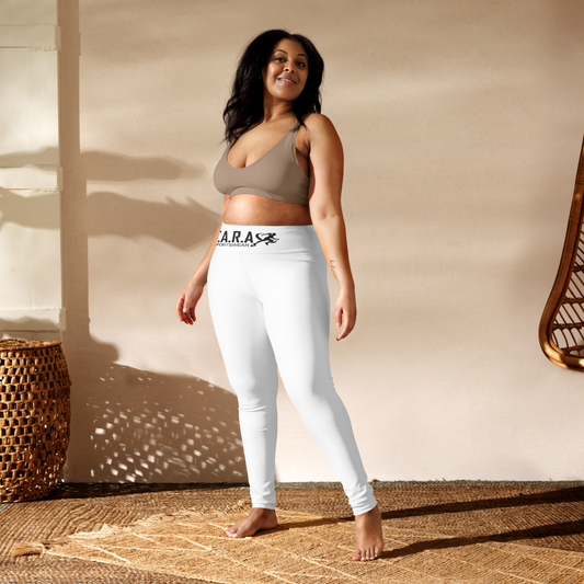 Woman wearing a sports bra and white leggings with a brand logo, standing against a neutral wall.