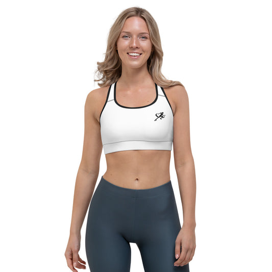 A woman wearing a white padded sports bra with a logo on the left chest area, paired with dark sports leggings.