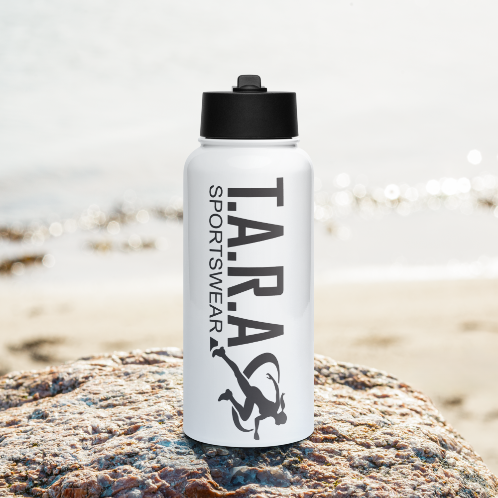 A white 32 oz (950 ml) water bottle with a black plastic lid and a wide-mouth foldable straw, lying on a rocky surface with a blurred background.