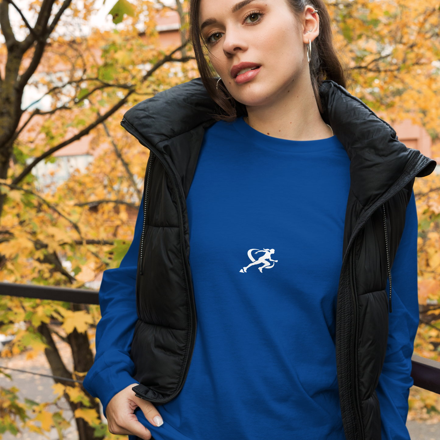 A woman wearing a blue long-sleeved crew neck t-shirt with a small white logo on the chest.