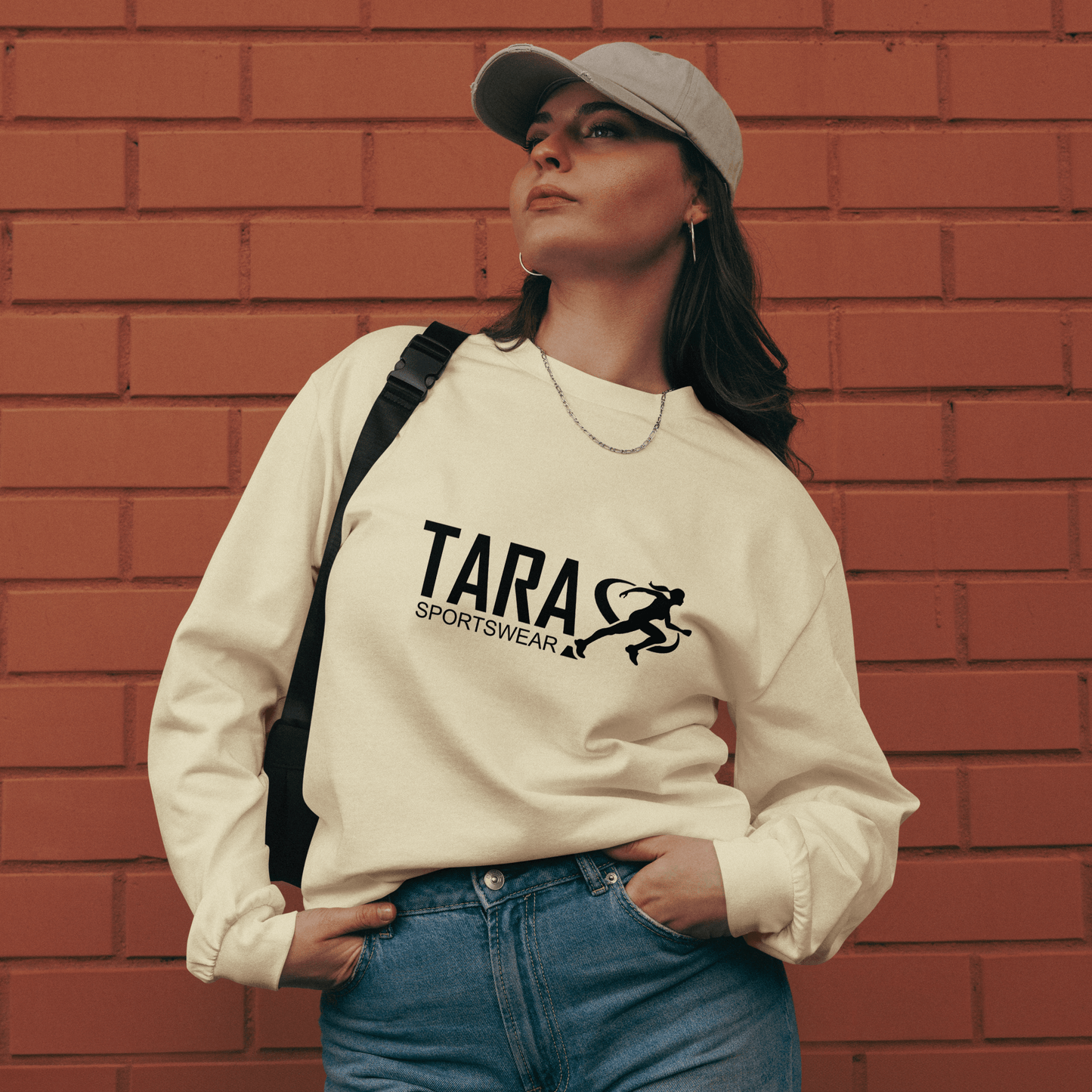 Person wearing a white sweatshirt with 'TARA SPORTSWEAR' logo against a brick wall.