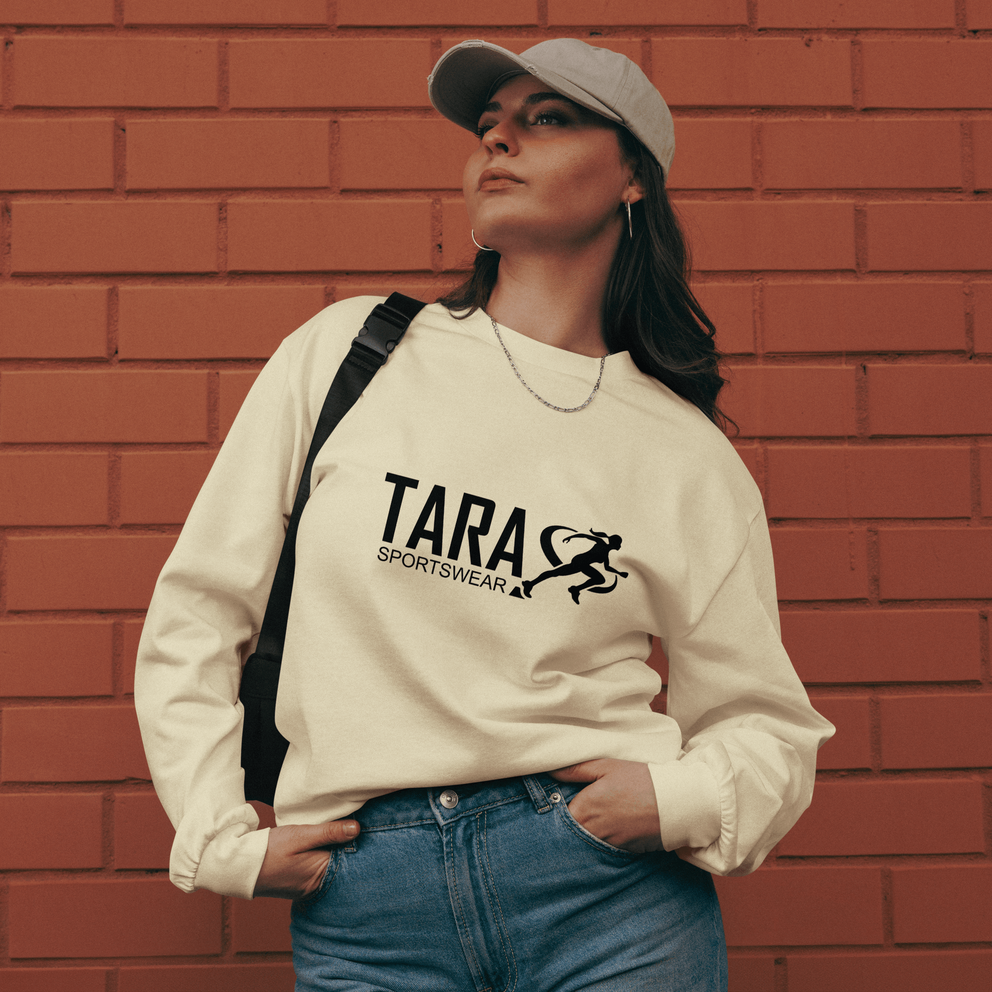 Person wearing a white sweatshirt with 'TARA SPORTSWEAR' logo against a brick wall.