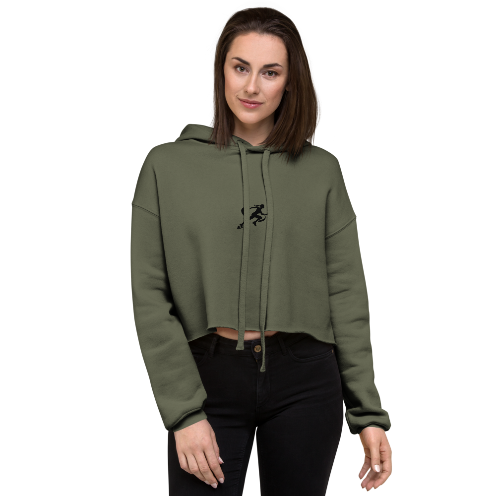 A woman wearing a military green cropped hoodie with a graphic on the front standing against a neutral background.