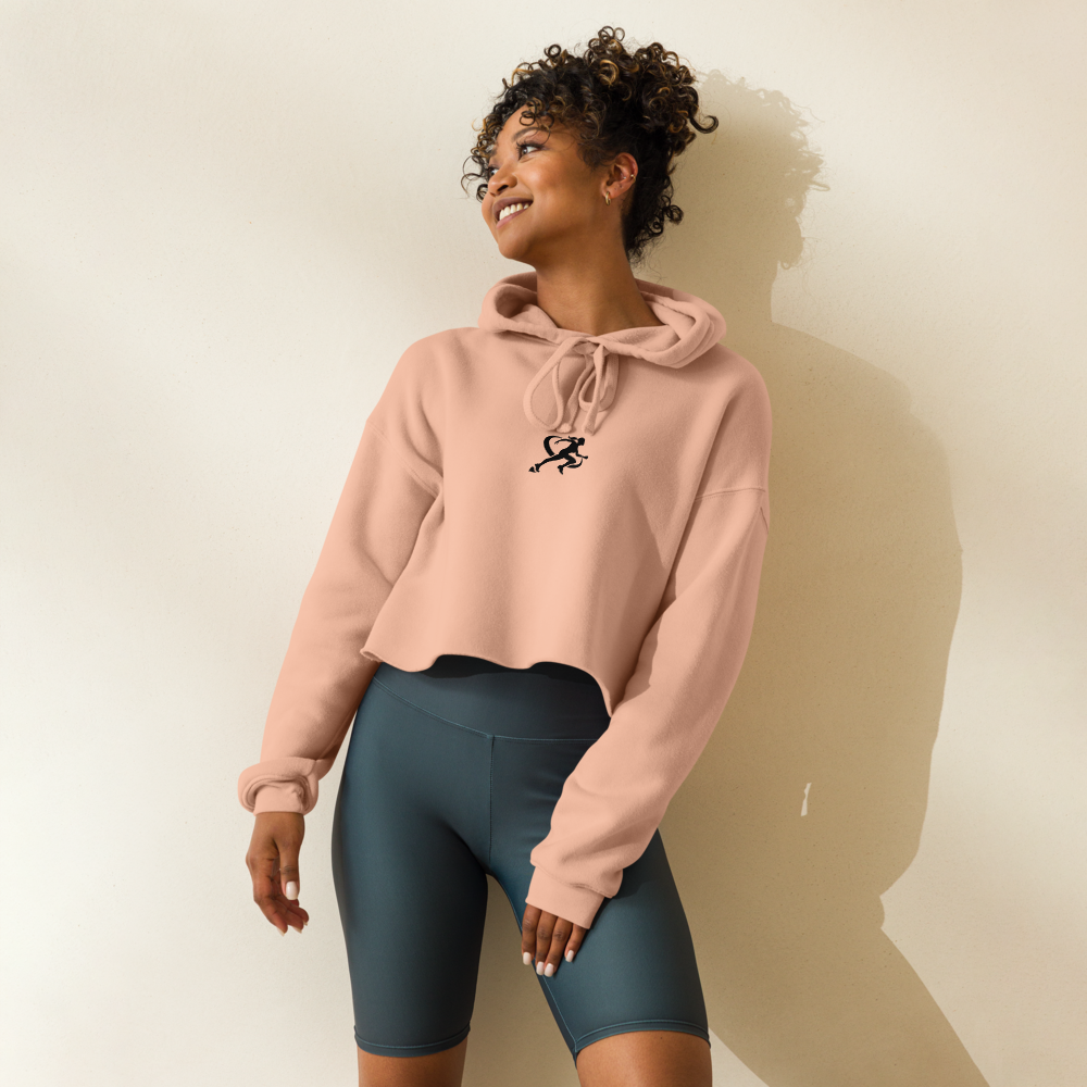 A woman wearing a beige cropped hoodie with a graphic on the front and matching gray leggings, standing against a neutral background.